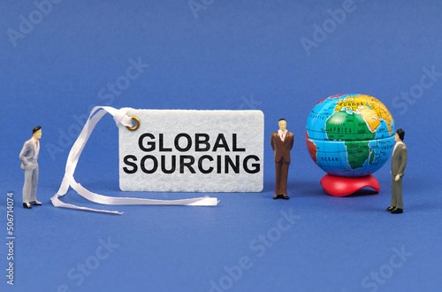 On the blue surface there are figurines of people, a globe and a white plate with the inscription - GLOBAL SOURCING photo