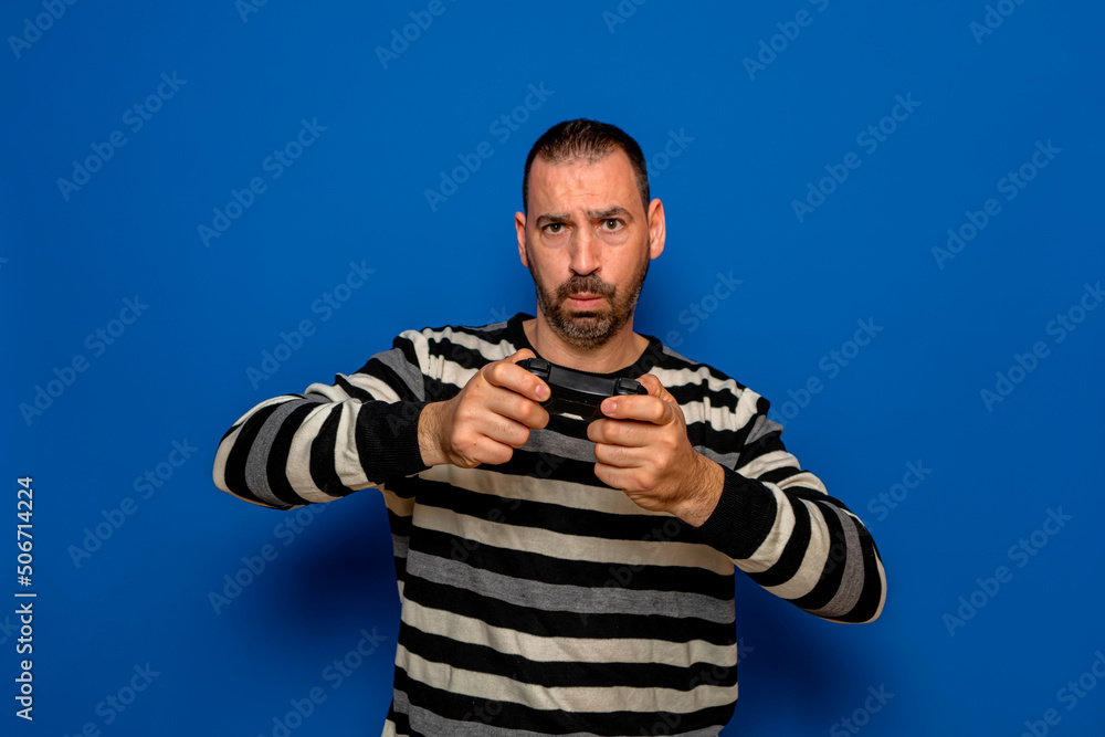 Portrait of concentrated bearded Caucasian man playing video games with a controller in his hands, isolated on blue studio background Portrait of concentrated bearded Caucasian man playing video games with a controller in his hands, isolated on blue studio background