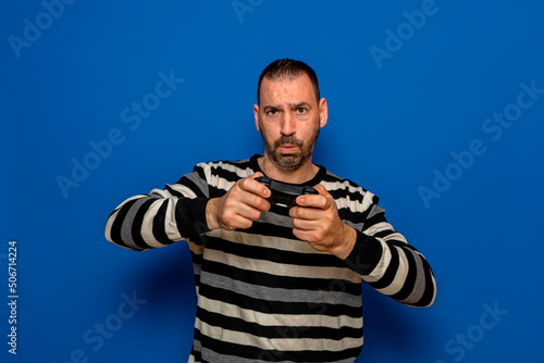 Portrait of concentrated bearded Caucasian man playing video games with a controller in his hands, isolated on blue studio background