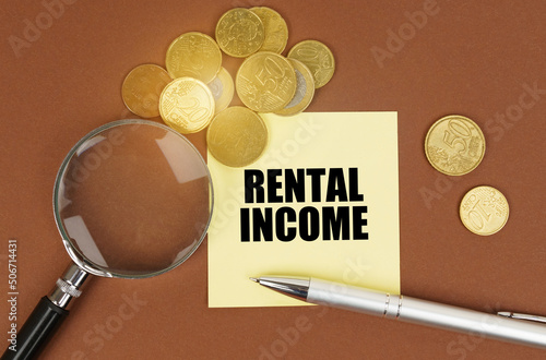 On a brown surface are coins, a pen, a magnifying glass and stickers with the inscription - Rental income