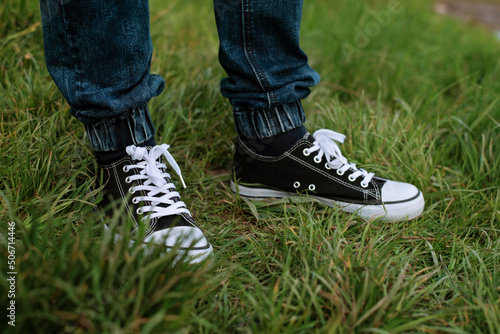 Sports shoes for running, brisk walking, close up. Sports shoes and blue jeans on the feet of a young man, a man standing in the grass while walking in nature
