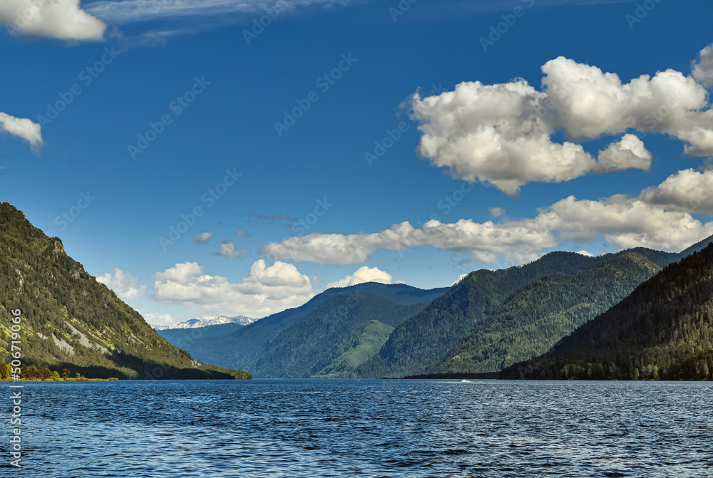 The beautiful lake is surrounded by majestic mountains. Blue sky and snow-white clouds.