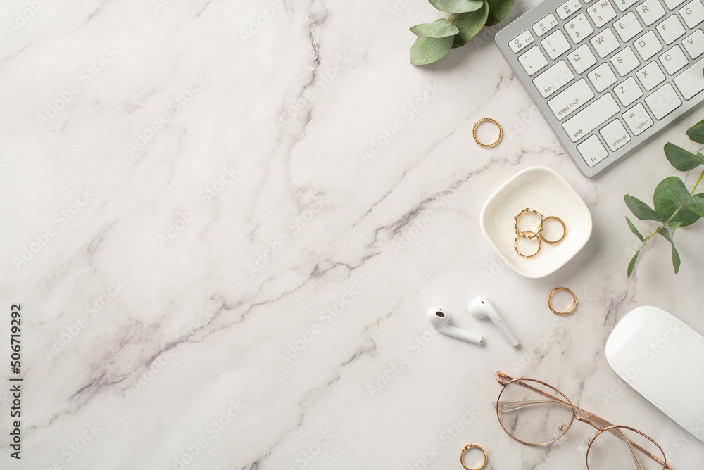 Business concept. Top view photo of workspace keyboard computer mouse wireless earbuds gold rings stylish glasses and eucalyptus on textured white marble background with copyspace