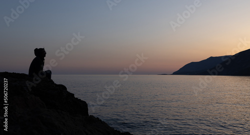 a man sits on a high seashore and watches the sunset, Greece, Crete, Chania