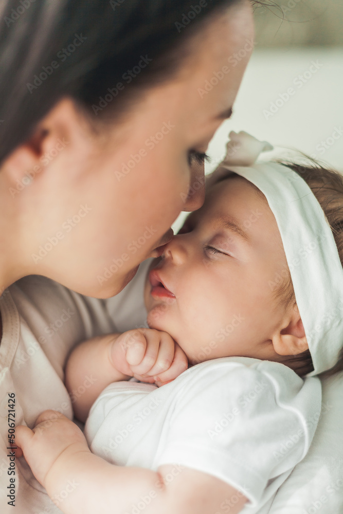 Close portrait of a little cute dark-haired newborn girl in a white suit in the arms of a young mother. Motherhood. Parent. Healthy sleep. Close portrait of a little cute dark-haired newborn girl in a white suit in the arms of a young mother. Motherhood. Parent. Healthy sleep.