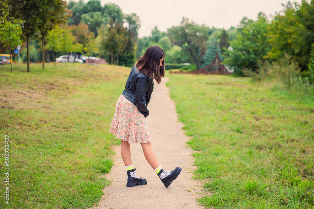 a slender dark-haired girl examines her shoes while standing on a path in the park a slender dark-haired girl examines her shoes while standing on a path in the park
