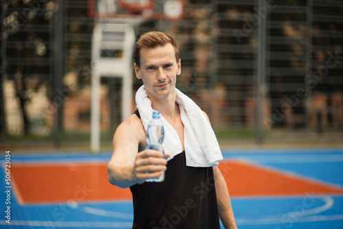 Sweaty guy opening cap of bottle to drink water after workout. Man drinking water after running. Portrait ff handsome athletic male in black sportswear resting after fitness workout