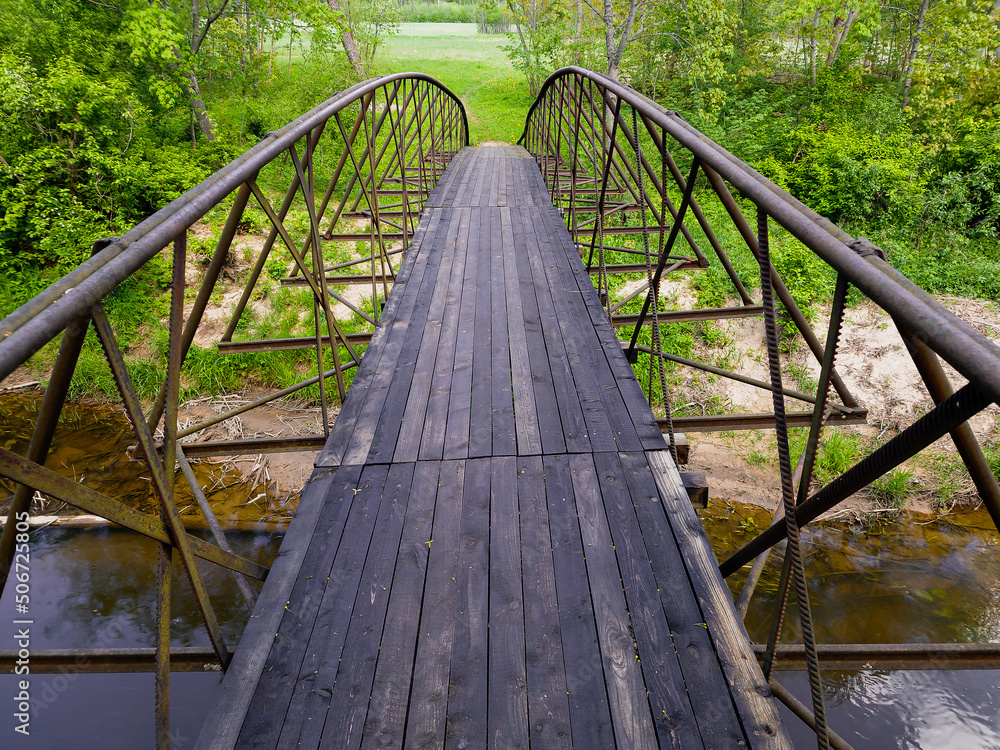 Obraz premium Pedestrian wooden bridge with railings over Ciecere river, Latvia.