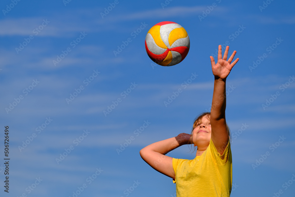 A girl is playing volleyball . The child hits the ball with his hand . Outdoor play.