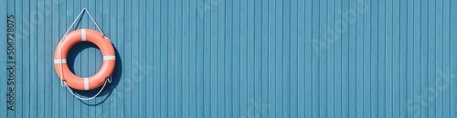 An orange lifebuoy hangs from a white cord on a sky blue wooden background. The concept of safety of people on the water, river, sea, ocean. Decorative nautical style