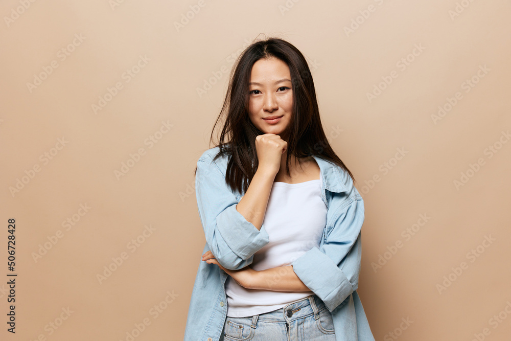 Cute smiling thoughtful tanned adorable young Asian lady reclines on hand fist posing isolated on beige pastel background. People and Emotions concept. Copy Space Offer Banner. Cute smiling thoughtful tanned adorable young Asian lady reclines on hand fist posing isolated on beige pastel background. People and Emotions concept. Copy Space Offer Banner.