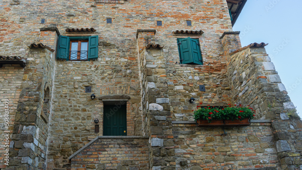 Traditional brick-style building in Italy, with green shutters and flowers.