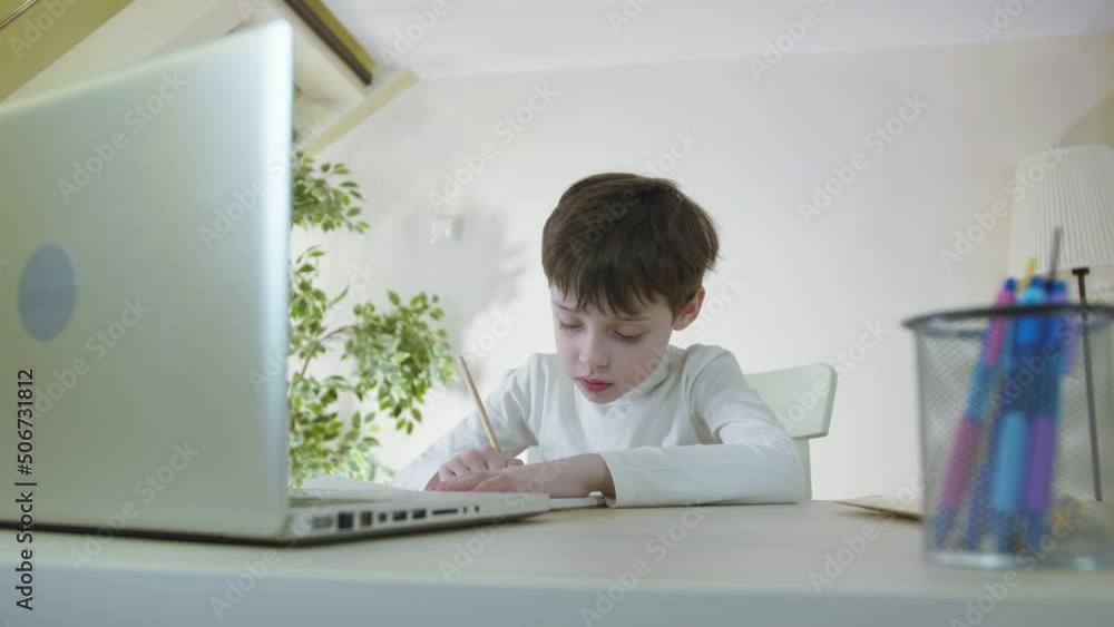 Focused Cute School Boy Studying at Table doing homework Listening Tutor by Video Call Elearning Drawing on Paper. Children Remote Education on the Quarantine Concept Focused Cute School Boy Studying at Table doing homework Listening Tutor by Video Call Elearning Drawing on Paper. Children Remote Education on the Quarantine Concept