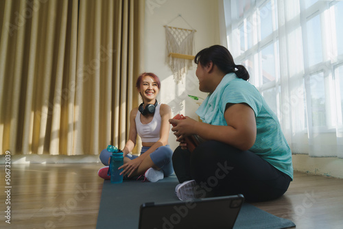Two Asian women's body size is different in sportswear sitting to enjoy talking relax on yoga mat. after fitness exercise at home together.  Healthy lifestyle with friends at home.
