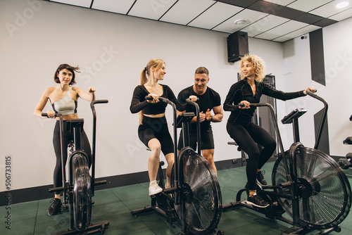 Young women make exercising on air bikes at gym with trainer motivating.