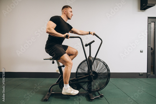 Strong man using air bike for cardio workout at cross training gym.