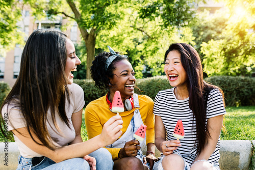 Cheerful multiethnic group of female friends talking and having fun together - Diverse tourist women eating watermelon ice cream while having fun on summer vacation - Happiness and friendship concept