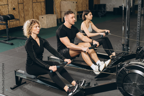 Young man and beautiful women working out with rowing machine at crossfit gym.