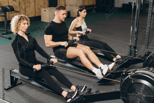 Fototapeta Naklejka Na Ścianę i Meble -  Young man and beautiful women working out with rowing machine at crossfit gym.