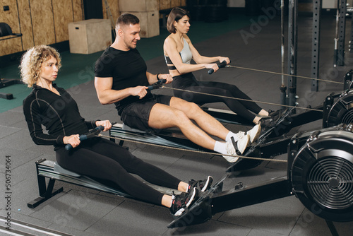 Young man and beautiful women working out with rowing machine at crossfit gym.