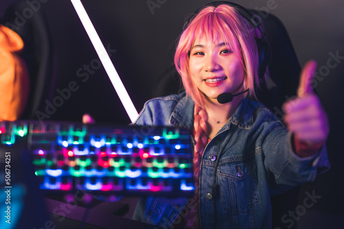 Young Asian female player in headphones showing illuminated keyboard and thumb up copy space concept . High quality photo