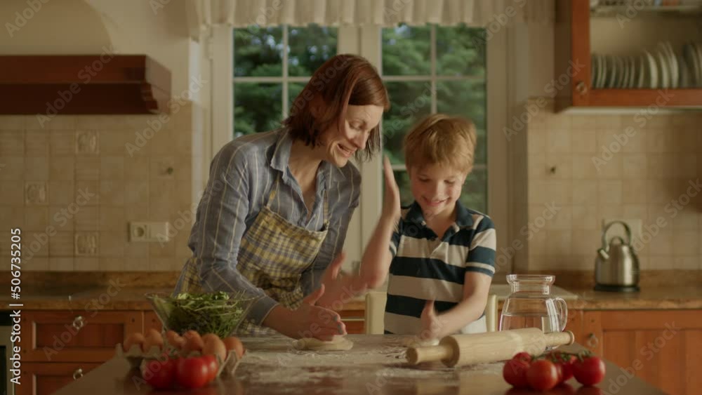 Young mother and cute kid kneading dough together standing in the kitchen. Happy family cooking homemade pizza. Young mother and cute kid kneading dough together standing in the kitchen. Happy family cooking homemade pizza.