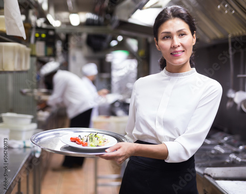 portrait of smiling female waiter standing in kitchen in restaurante photo