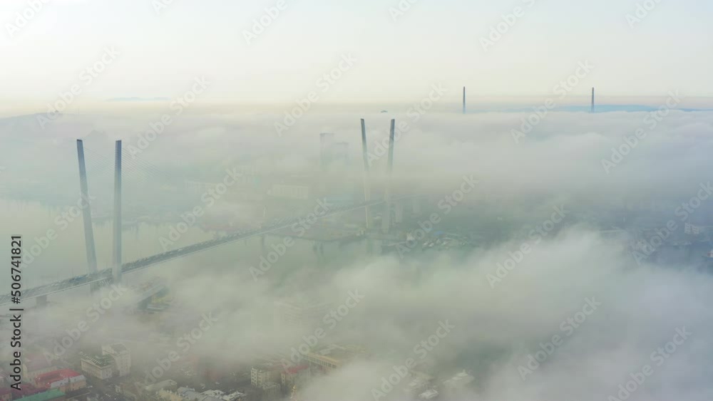 Golden bridge and Russian bridge at dawn mist in Vladivostok city. The tops of the pylons are visible. Modern cable-stayed construction. The largest suspension bridges in Russia. Drone view Golden bridge and Russian bridge at dawn mist in Vladivostok city. The tops of the pylons are visible. Modern cable-stayed construction. The largest suspension bridges in Russia. Drone view