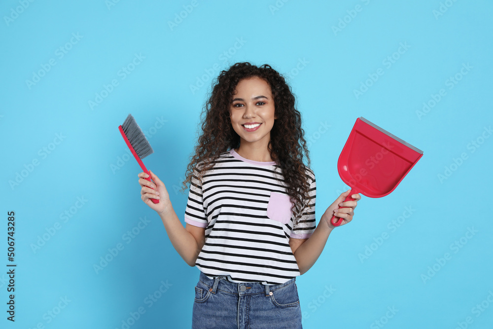 African American woman with broom and dustpan on light blue background African American woman with broom and dustpan on light blue background