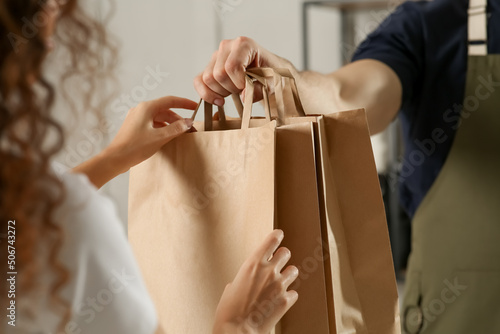 Worker giving paper bags to customer indoors, closeup
