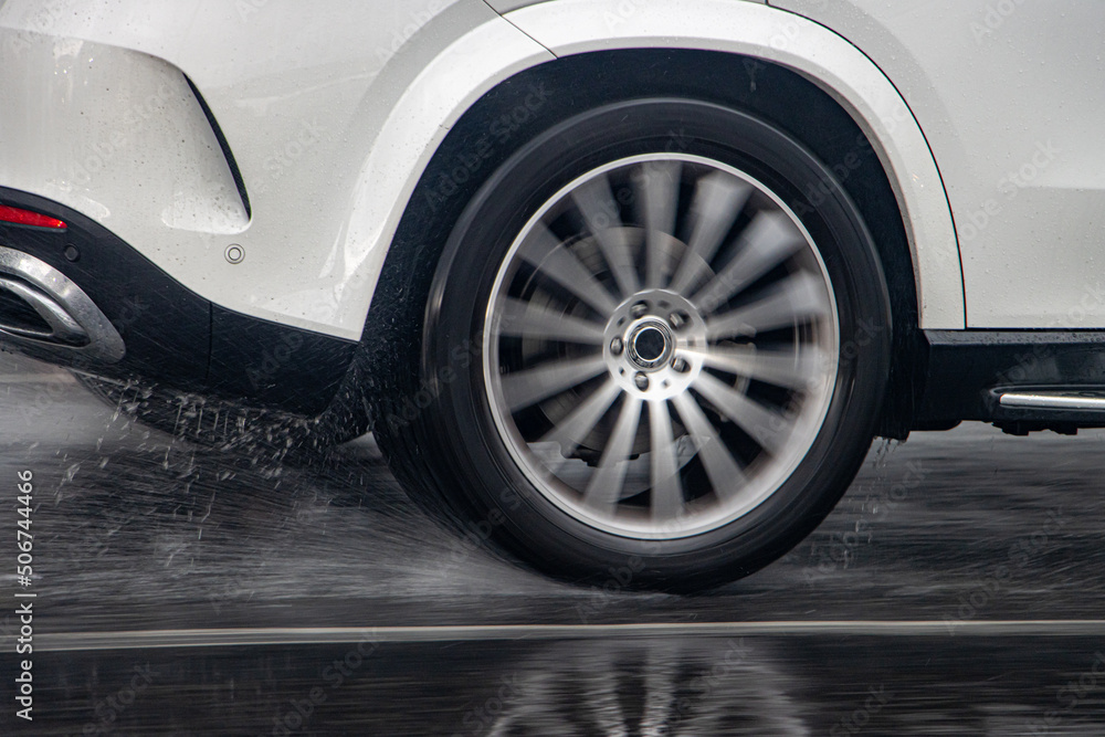 Detail of the rear wheel of a car driving in the rain on a wet road.