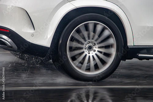Detail of the rear wheel of a car driving in the rain on a wet road. © milkovasa