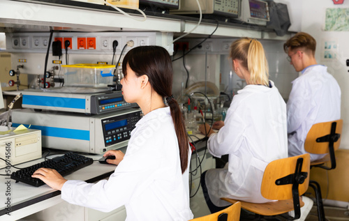 Portrait of young Chinese woman lab technician engaged in research in chemical laboratory with her colleagues