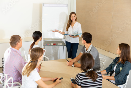 Positive young female business coach communicating with adult auditorium during training in office