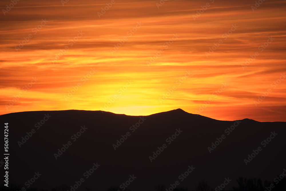 Beautiful evening panoramic landscape with bright setting sun over distant mountain peaks at sunset