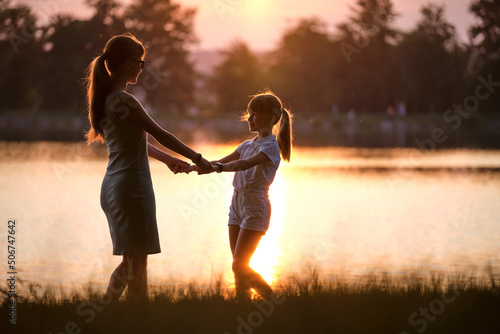 Happy mom and daughter girl relaxing holding hands enjoying time together in summer park at sunset. Family love and relationship concept