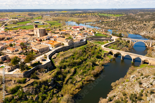 Scenic drone view of historic center of Ledesma town on banks of Tormes river surrounded by ancient defensive wall on sunny spring day on background of large natural rural landscape, Salamanca, Spain