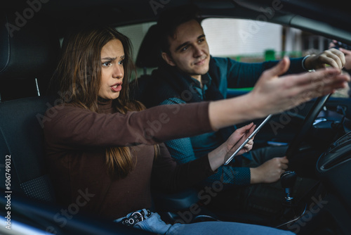 Man and woman young couple or friends male and female boyfriend and girlfriend using digital tablet for navigation searching map for direction arguing while travel in car real people copy space