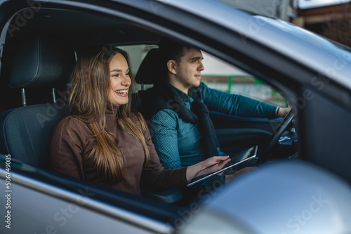 Man and woman young couple or friends male and female boyfriend and girlfriend happy smile using digital tablet for navigation searching map for direction while travel in car real people copy space