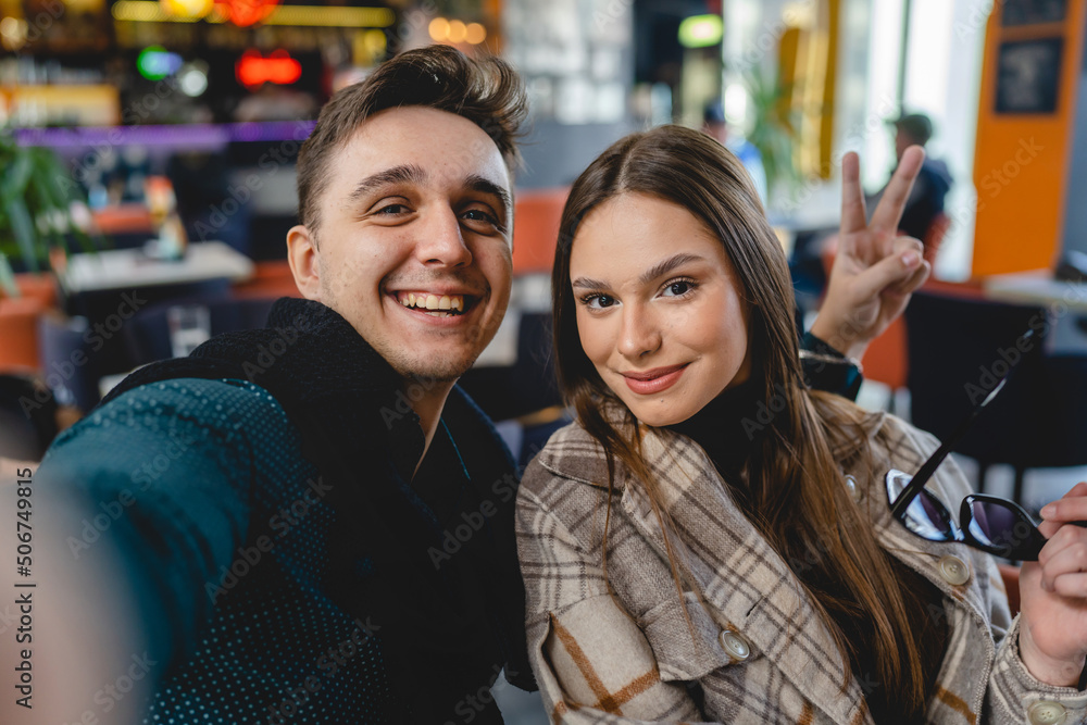 Two people young caucasian couple man and woman female and male friends or boyfriend and girlfriend taking selfie photos or making a video call while sitting at cafe copy space fun and romance Two people young caucasian couple man and woman female and male friends or boyfriend and girlfriend taking selfie photos or making a video call while sitting at cafe copy space fun and romance