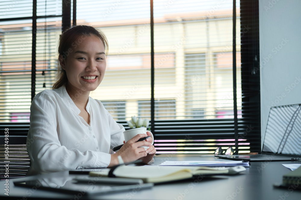 Positive young business woman holding coffee cup and smiling at camera. Positive young business woman holding coffee cup and smiling at camera.
