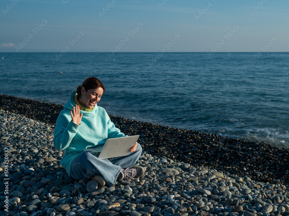 Caucasian woman communicating by video call on laptop on pebble beach. 