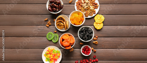 Bowls with different dried fruits and nuts on wooden background with space for text