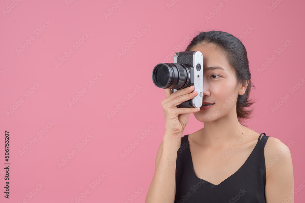 .Portrait of a young asian woman holding photo camera and looking away at copy space isolated over pink background. Female photography in action. .Portrait of a young asian woman holding photo camera and looking away at copy space isolated over pink background. Female photography in action.