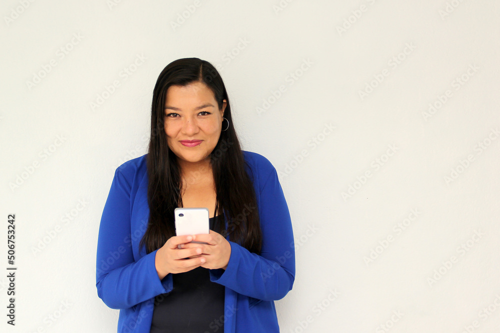 Latin adult woman with straight black hair and a blue jacket sends and receives messages from her cell phone very excited and happy makes purchases online in app

