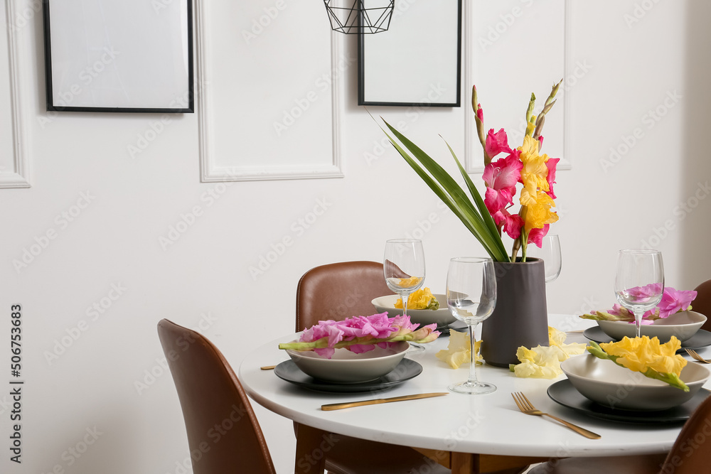 Dining table with stylish setting and beautiful Gladiolus flowers in light room