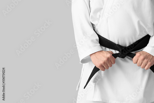 Man in karategi and with black belt on light background, closeup