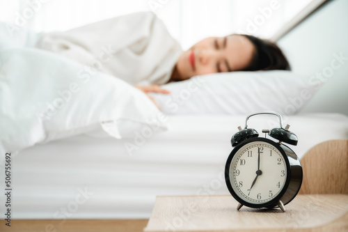 Young asian woman happy sleep at morning in bedroom. Closeup of alarm clock on white bed