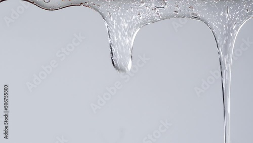 Closeup shot of transparent cosmetic gel fluid flowing on white background.
