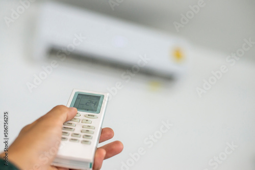 An air conditioner in a room with a young person using a remote control is turning on the air conditioner during the sweltering day at home.